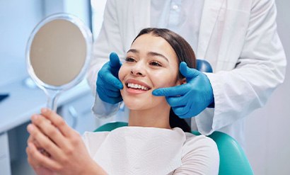 a patient smiling and checking her teeth with a mirror
