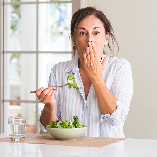 woman eating salad covering mouth