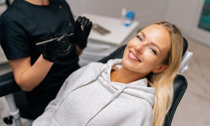 Woman in grey sweatshirt smiling while sitting in dental chair