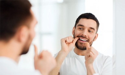Man smiling while flossing his teeth in bathroom