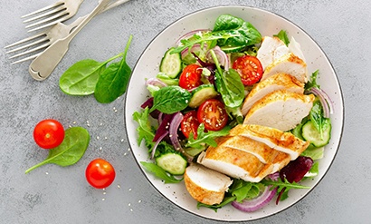 Bird’s eye view of garden salad with chicken next to utensils on a table