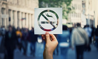 Hand holding cutout of “no smoking” symbol in front of a busy street of people