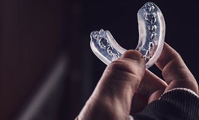 Thumb and forefinger holding a clear mouthguard with dark background