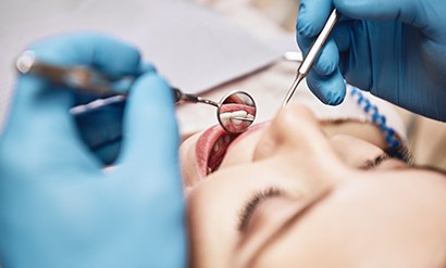Blue-gloved hands holding dental instruments during woman’s exam