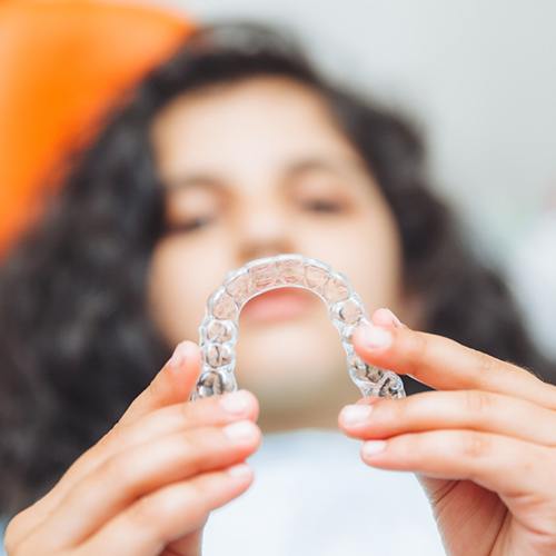 Teen in dental chair blurry in background holding Invisalign to foreground