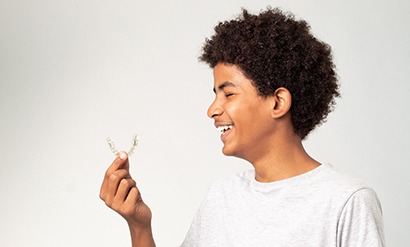Profile view of teen in t-shirt smiling with eyes closed holding Invisalign