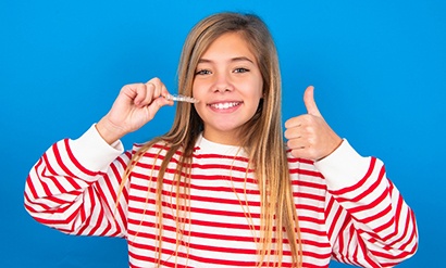 Girl in striped sweater holding Invisalign giving thumbs up