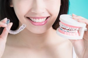 Woman holding Invisalign and fake teeth with braces