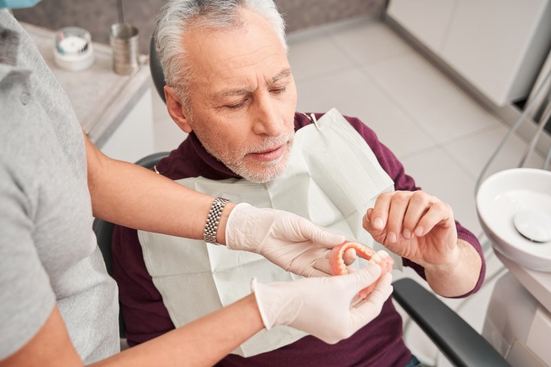 An older man talking to his dentist about his dentures