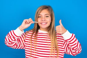 Teen in striped shirt holding Invisalign and giving thumbs up